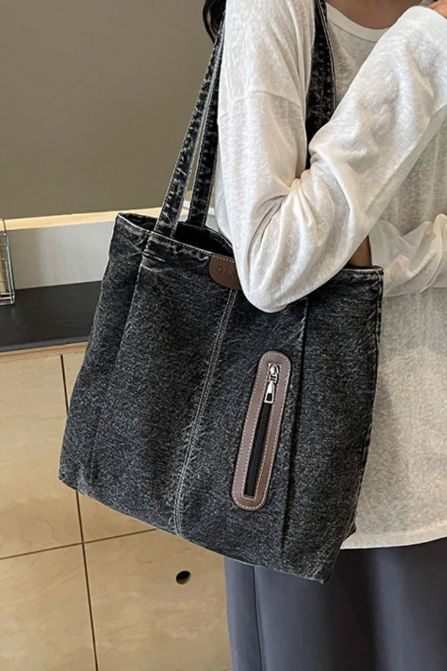 Dark denim tote bag with leather trim and zippered pocket.