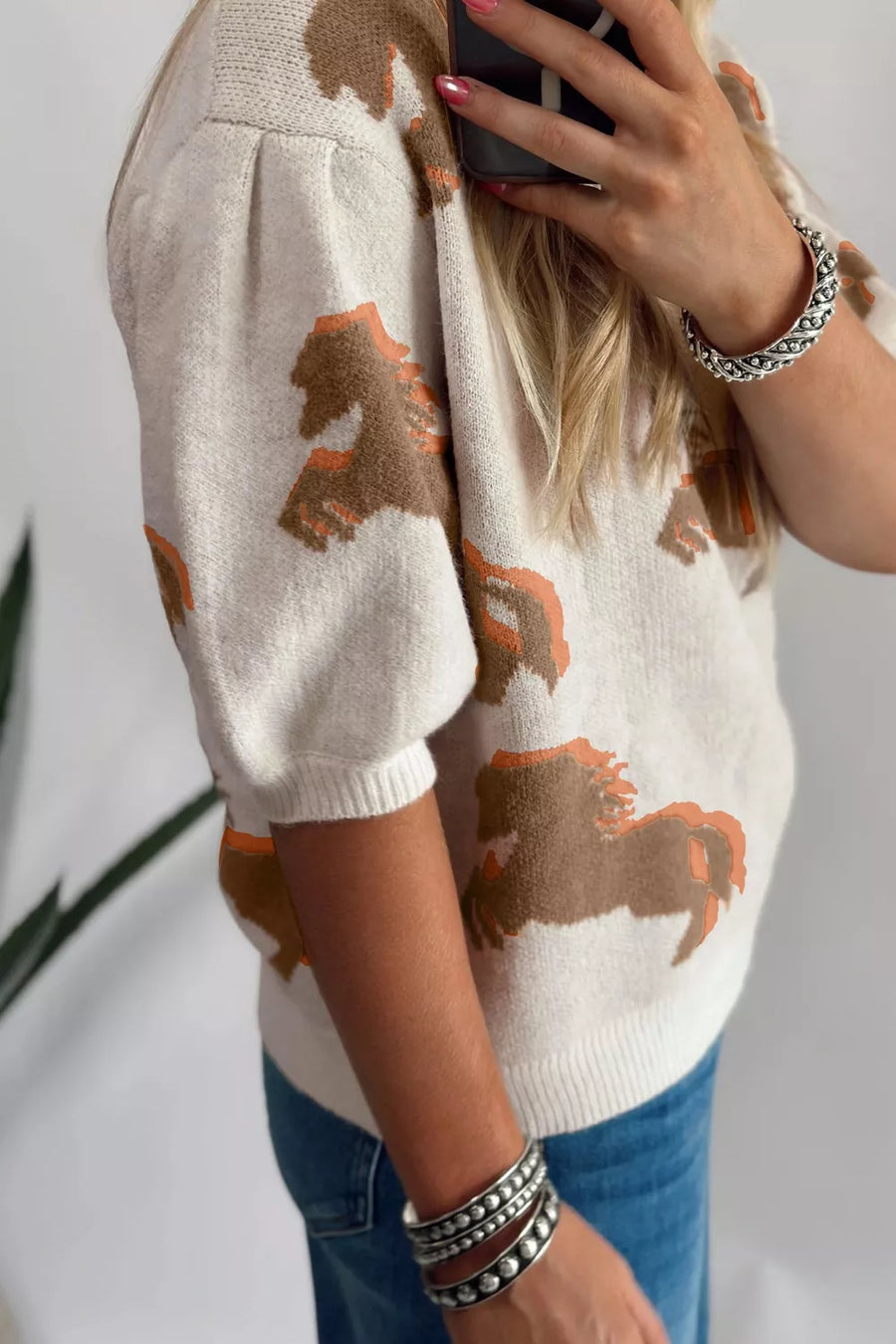 Beige knit sweater with puff sleeves and a horse print, styled with jeans and bracelets.