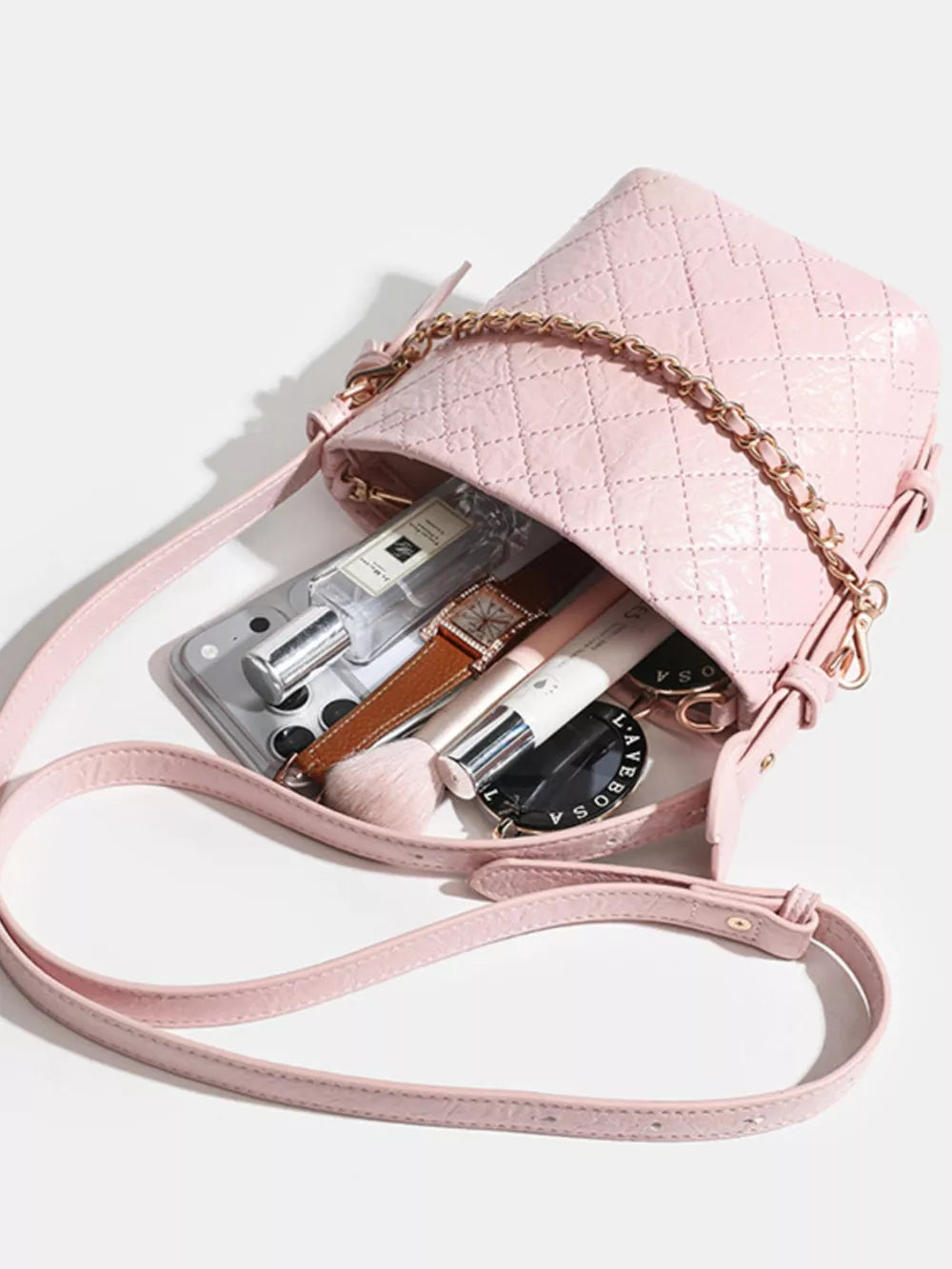 Pink quilted bucket bag with chain accent and leather strap, filled with makeup and accessories.
