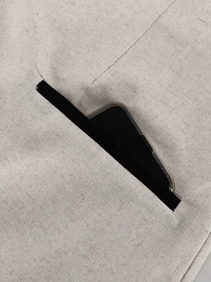 Linen blend trousers in beige with a black trim pocket holding a phone.