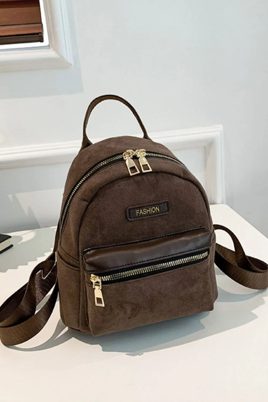 Coffee brown suede mini backpack with golden zips and "FASHION" detail.