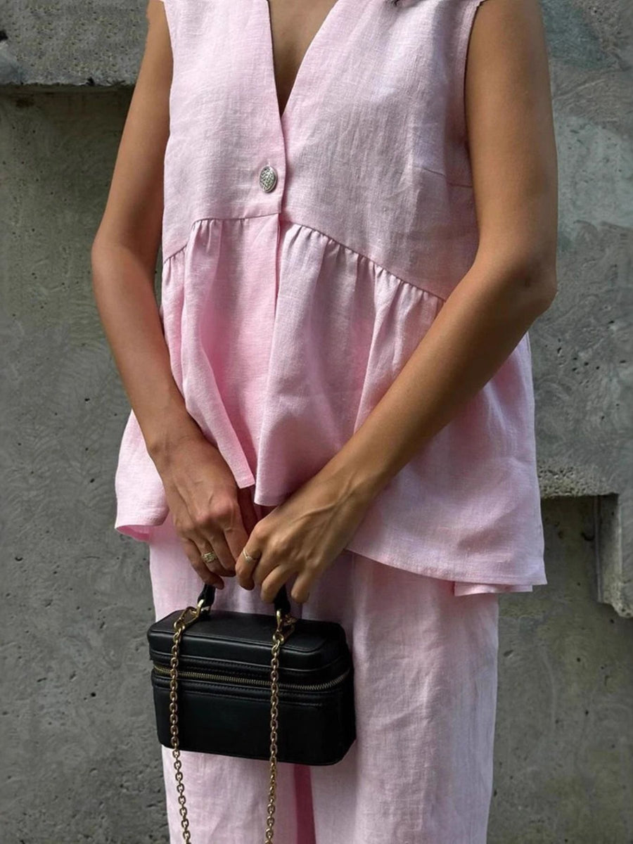 Sleeveless pink linen blend peplum top with V-neck and button detail, paired with wide-leg pants.