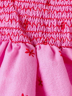 Pink cotton baby dress with smocked bodice and red floral print skirt.
