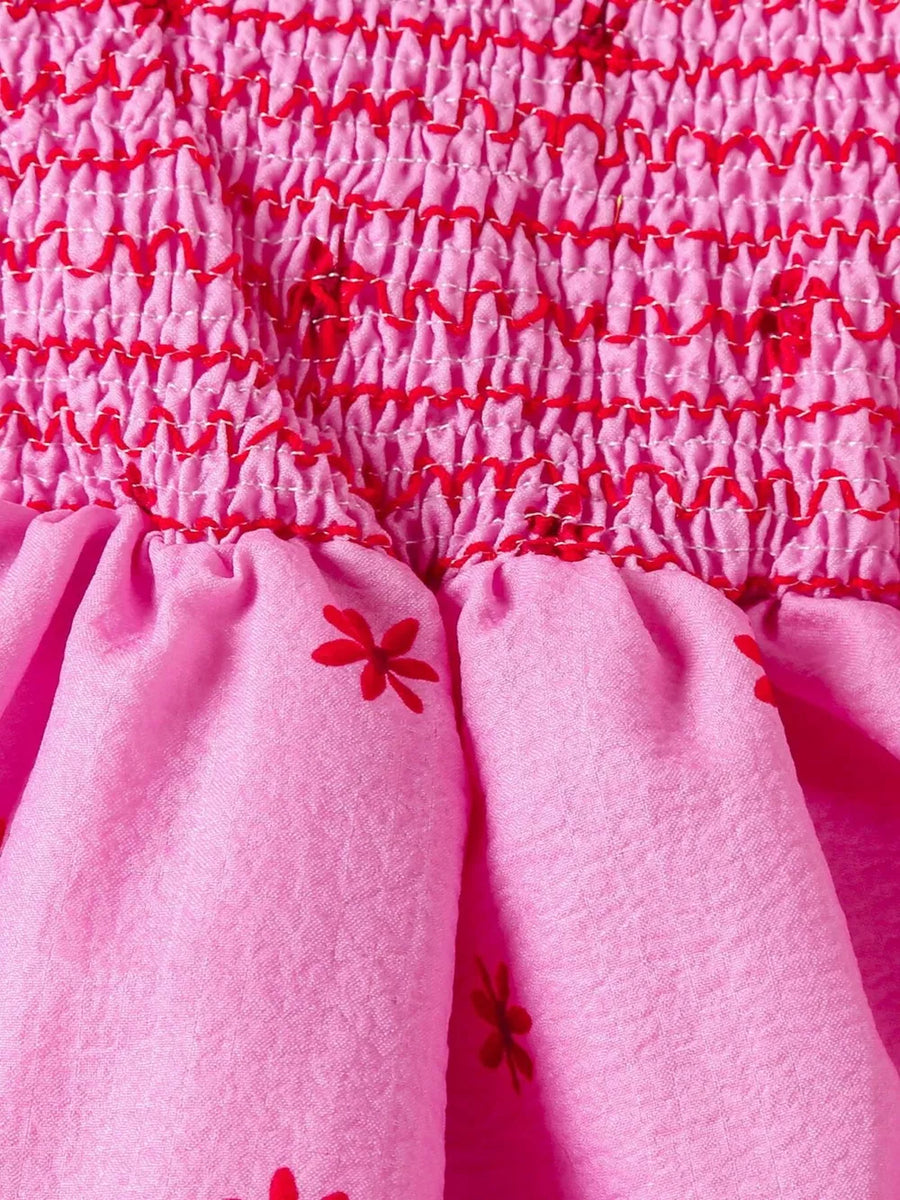 Pink cotton baby dress with smocked bodice and red floral print skirt.