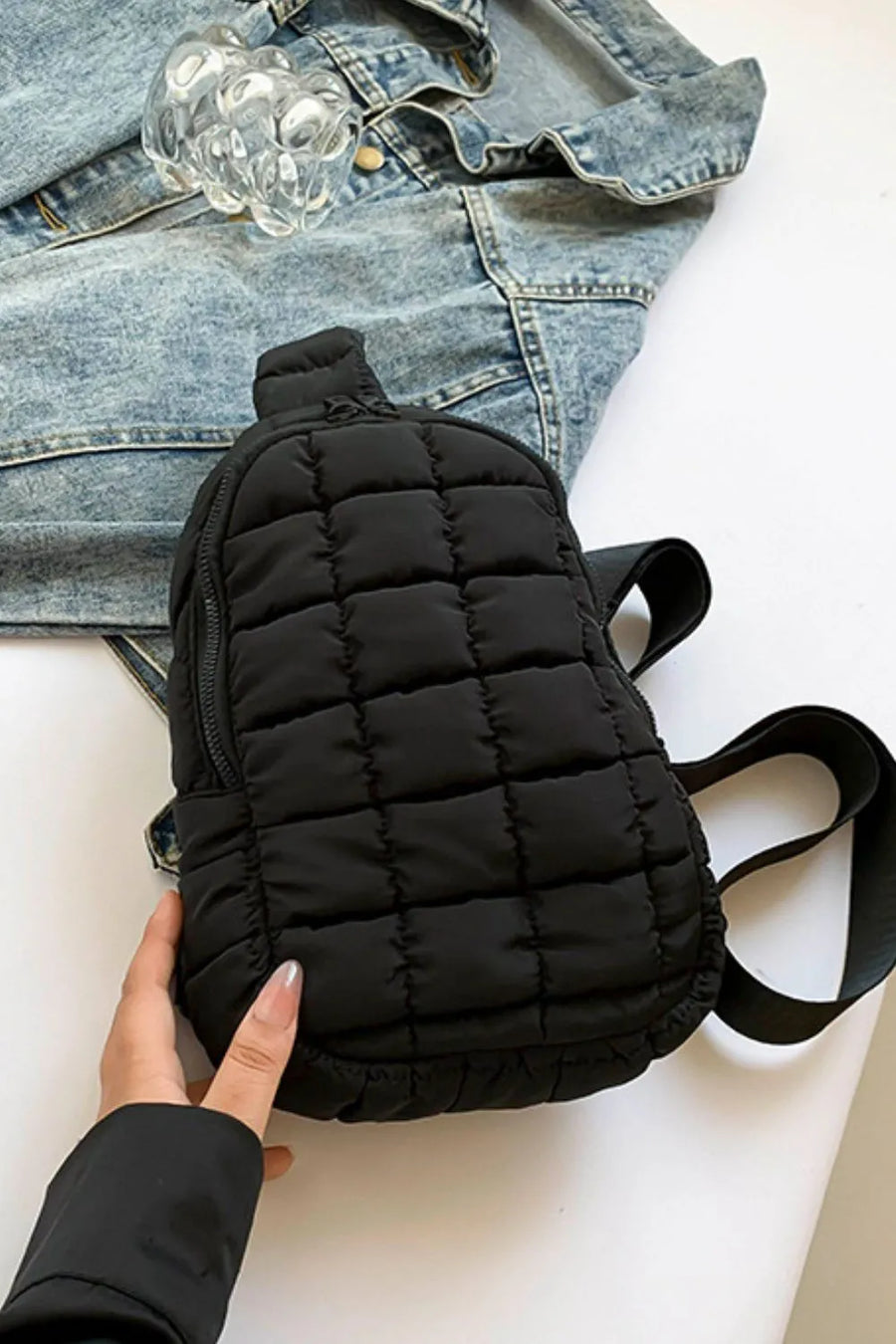 Black quilted sling bag with top handle and adjustable strap