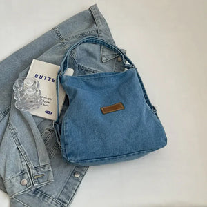 Medium wash denim hobo bag with leatherette patch and adjustable strap.