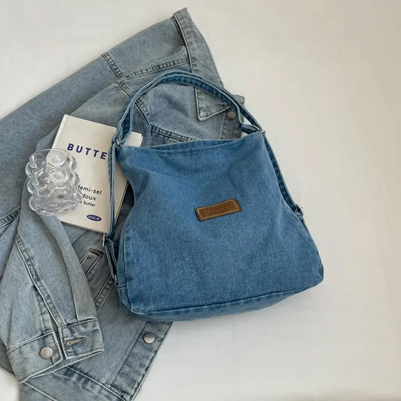 Medium wash denim hobo bag with leatherette patch and adjustable strap.