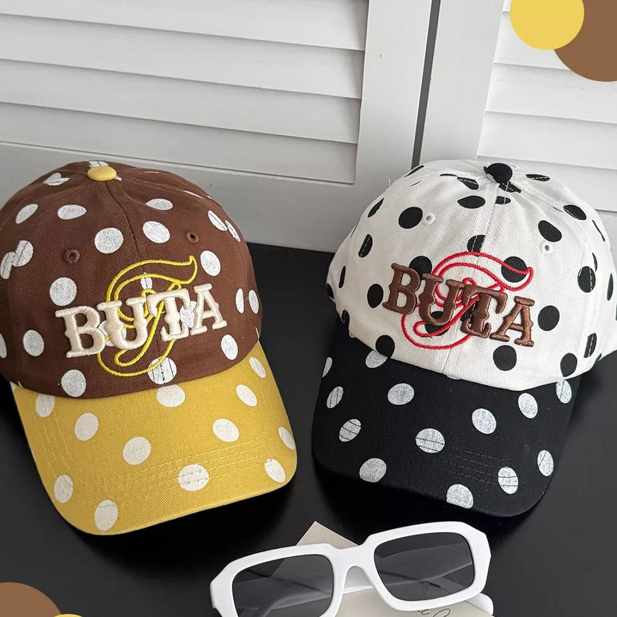 Polka dot baseball caps, one brown with yellow brim, one white with black brim, both embroidered with BUTA.