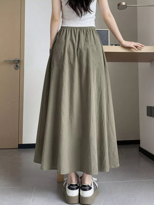 Olive green maxi skirt with pockets and elastic waist, shown on a woman wearing a white tank top.