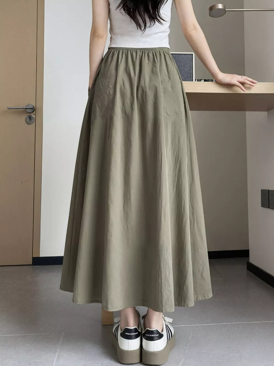 Olive green maxi skirt with pockets and elastic waist, shown on a woman wearing a white tank top.