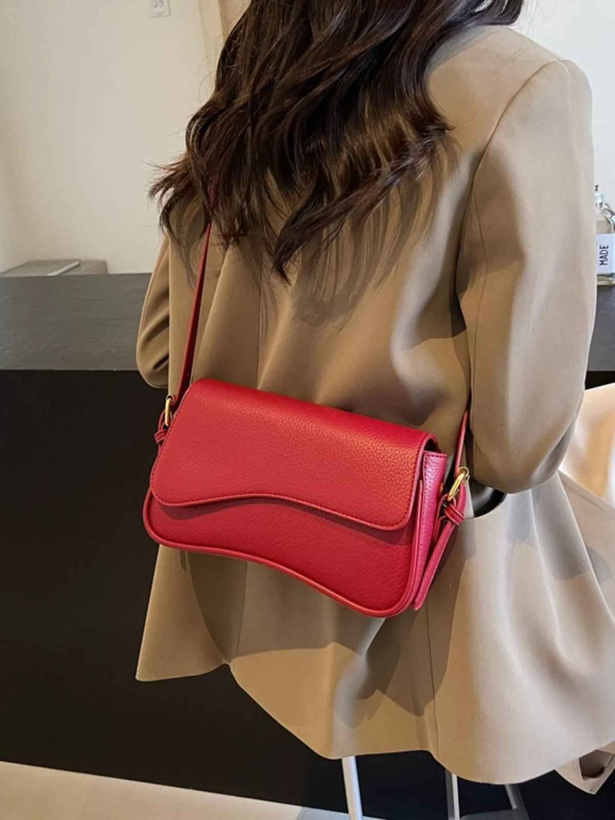 Red faux leather crossbody bag with a curved flap closure.