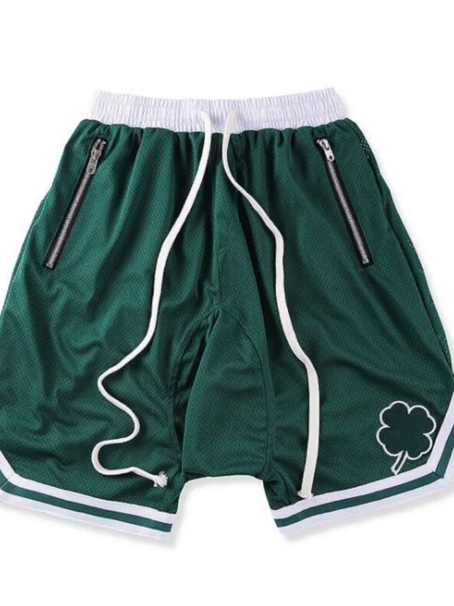 Dark green mesh basketball shorts with white drawstring, zipper pockets, and clover logo detail.