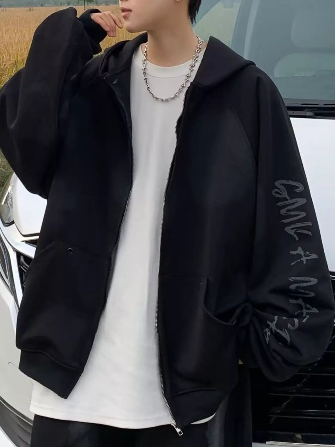 Black oversized zip-up hoodie with graphic print on sleeve, worn over white t-shirt.