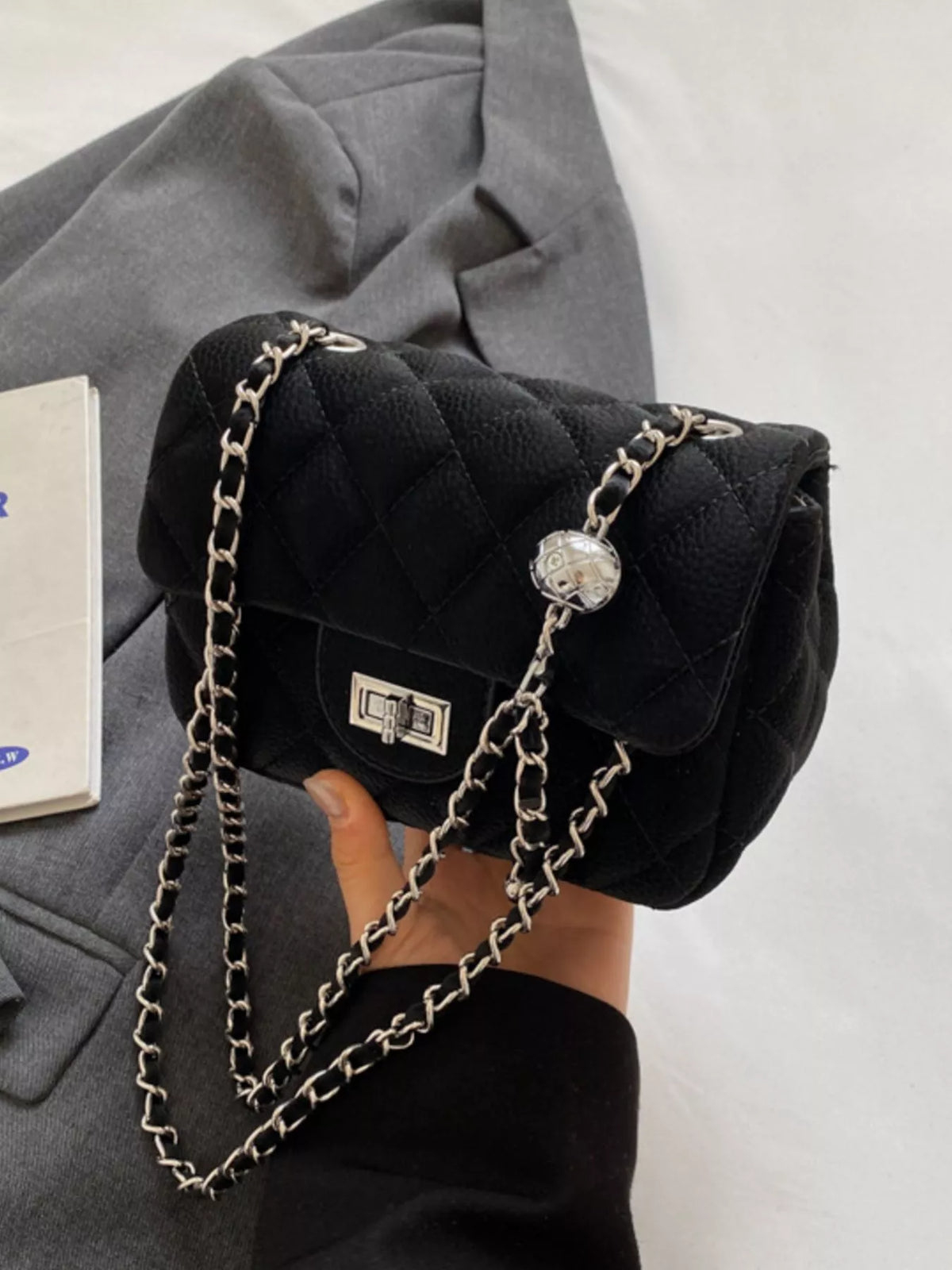 Black quilted chain crossbody clutch with silver hardware and decorative ball detail.