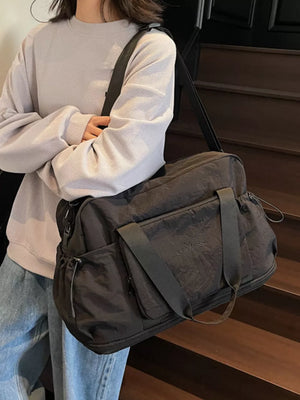 Black duffle bag with multiple pockets and shoulder strap, worn by a person in a grey sweater.