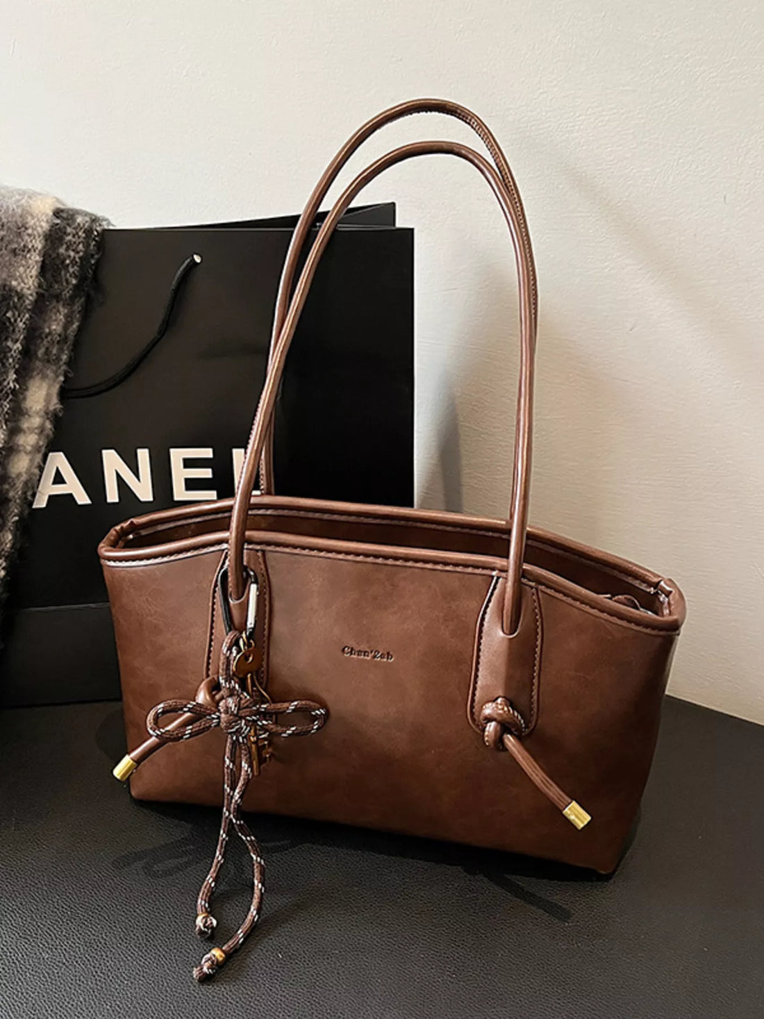Brown leather shoulder bag with braided tassel detail and gold hardware.
