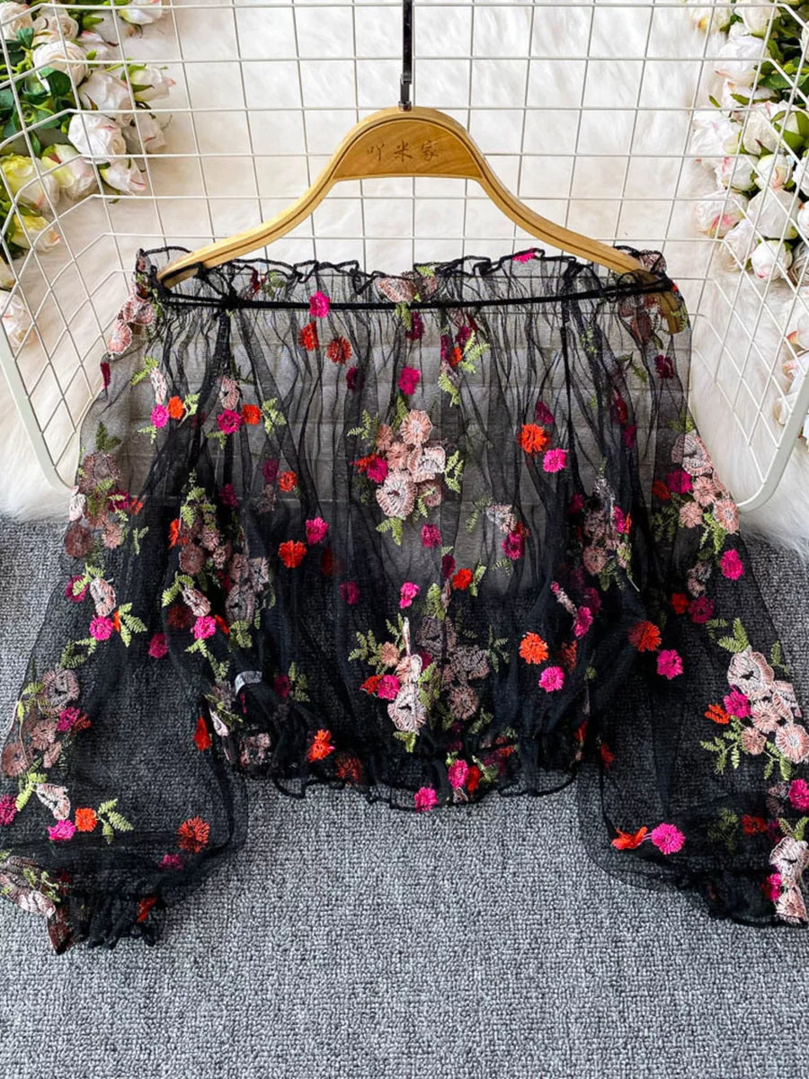 Black off-shoulder t-shirt with embroidered floral detail and ruffled neckline.