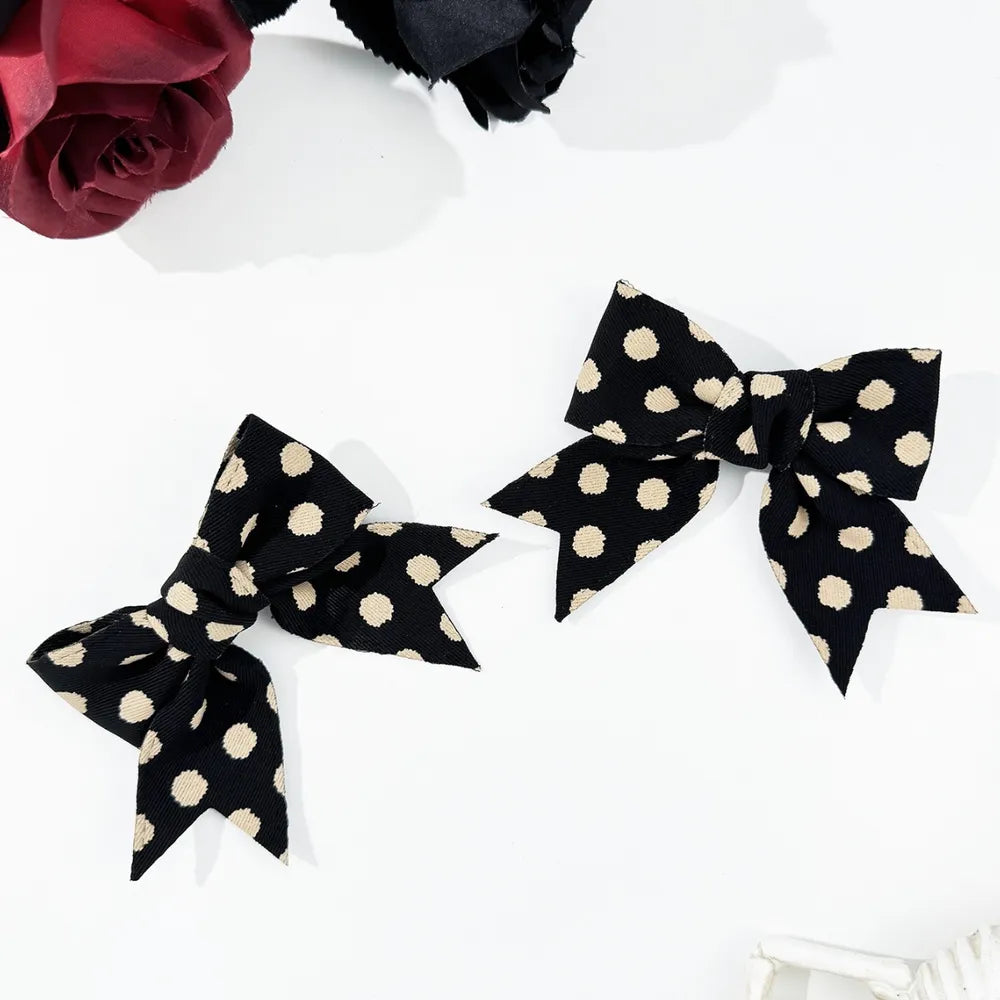 Black polka dot bow barrettes set with cream dots, two pieces.