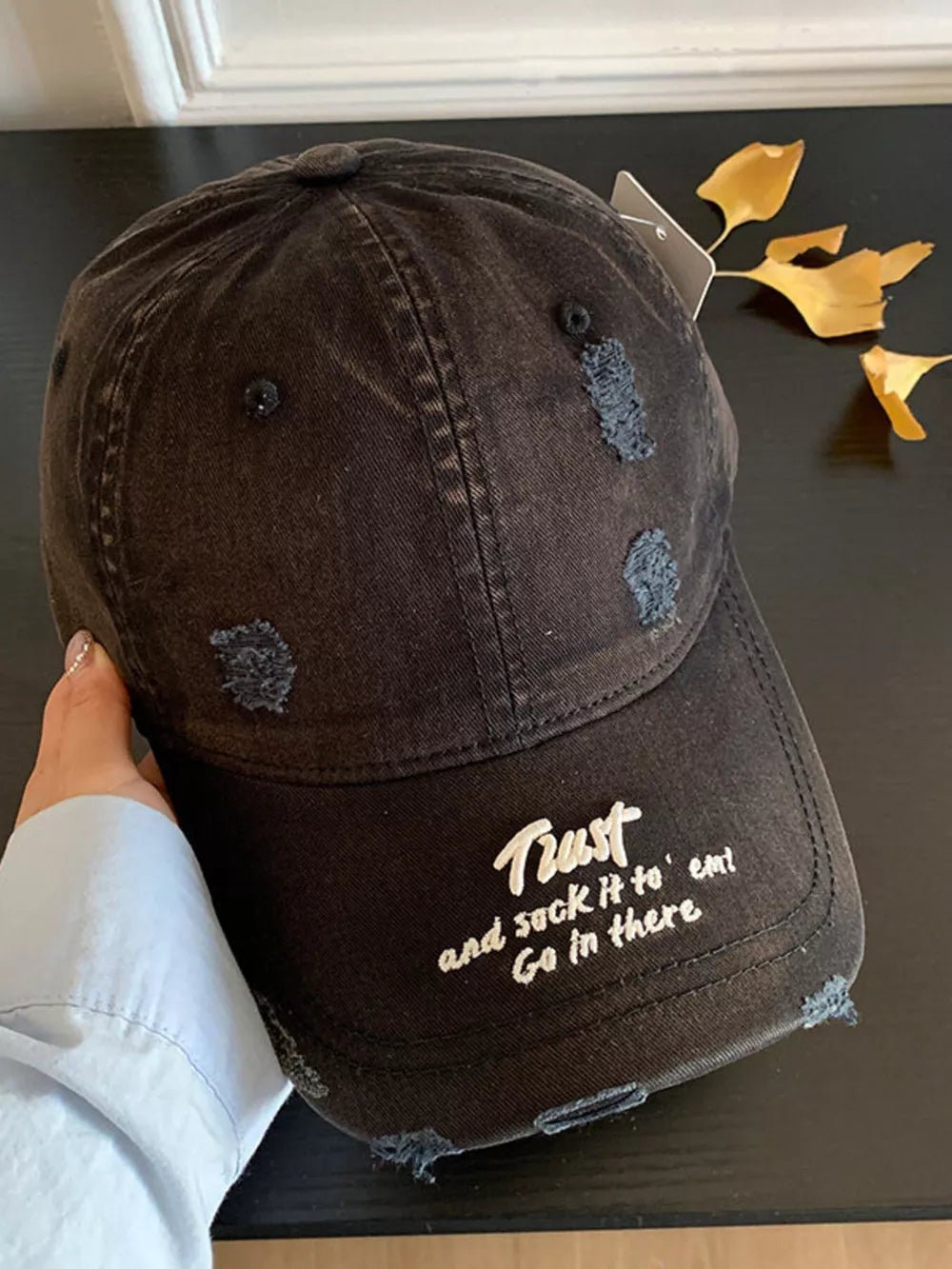 Black distressed baseball hat with white embroidered text and frayed details.
