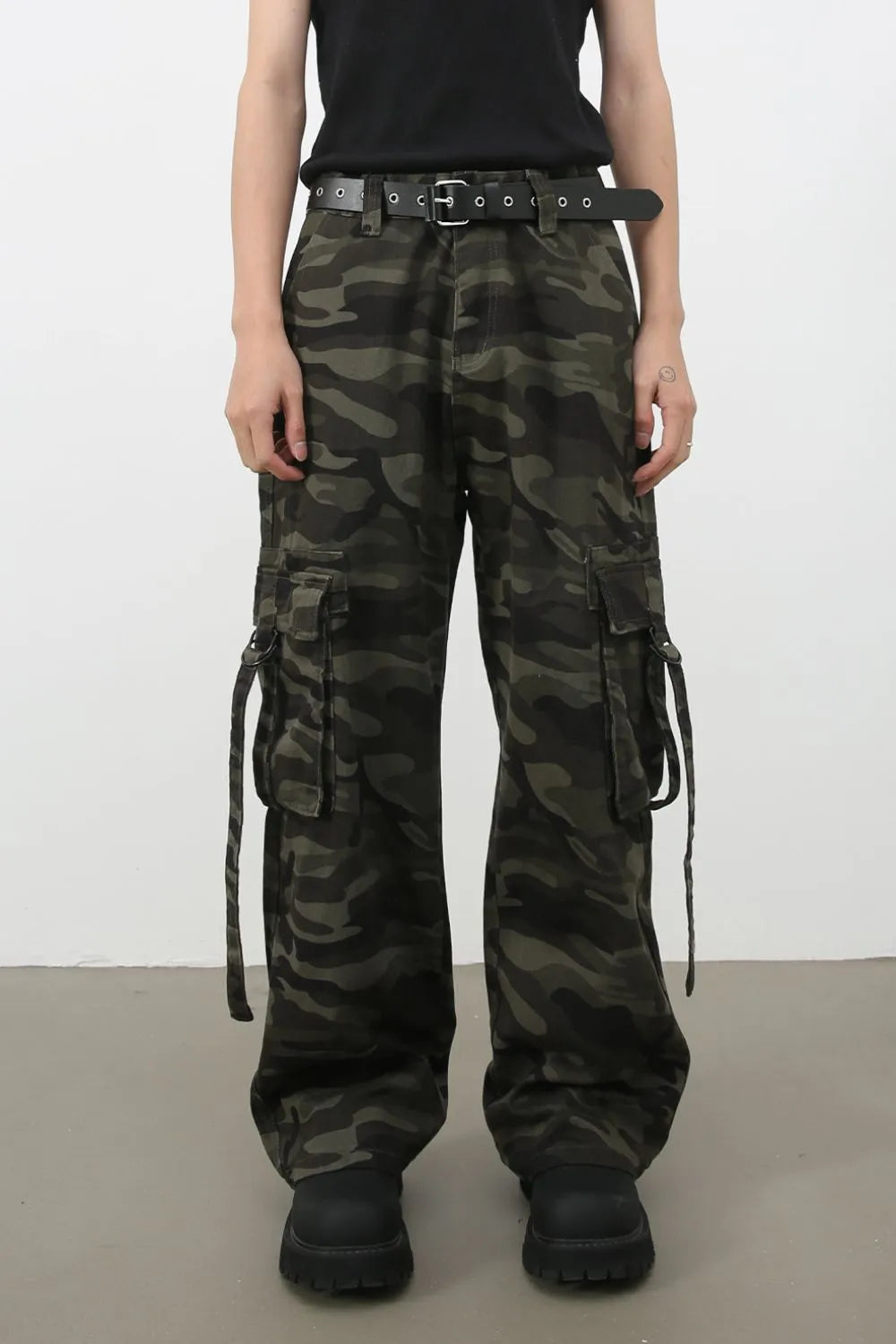 Wide-leg camo cargo pants in green camouflage with a black belted detail and multiple cargo pockets.