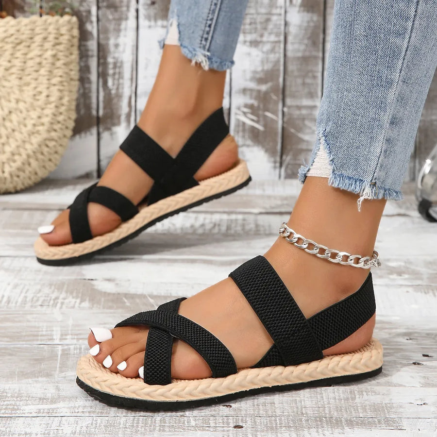 Black woven sole crossover sandals with elastic straps and a braided espadrille trim.
