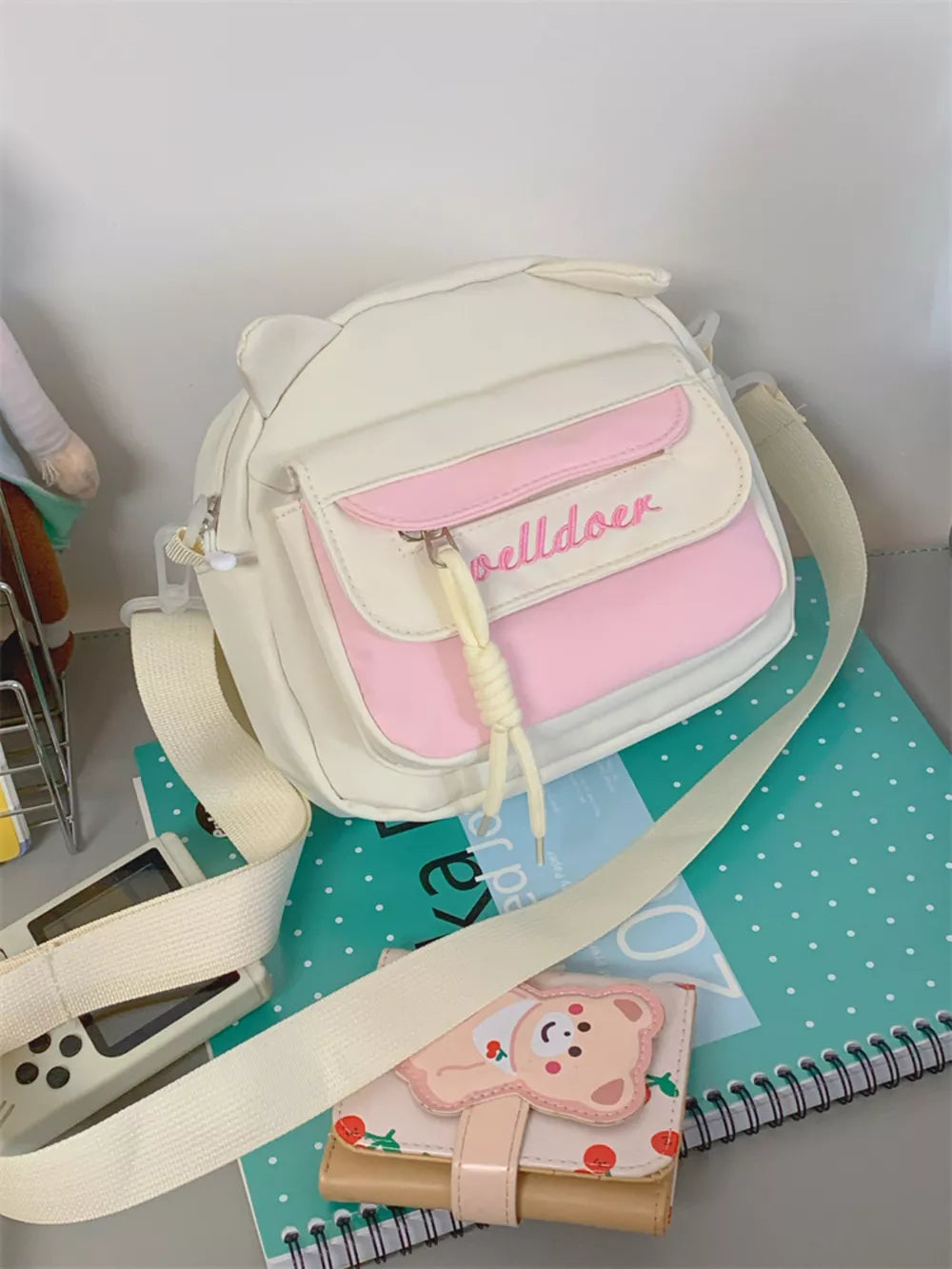 White and pink crossbody bag with cat ears and adjustable strap.