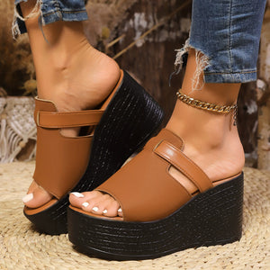 Light brown open-toe wedge sandals with black platform sole and ankle chain detail.