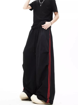 Relaxed wide-leg sweatpants in black with red side stripes and adjustable drawstring waist.