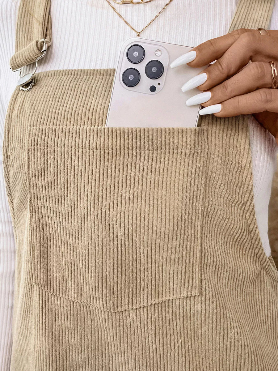 Tan corduroy overall dress with a large front pocket and metal strap clasps.