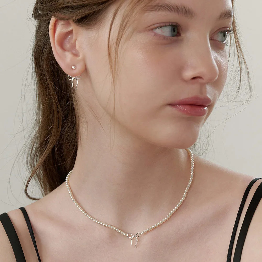 Delicate pearl choker necklace with silver bow pendant and matching stud earrings.