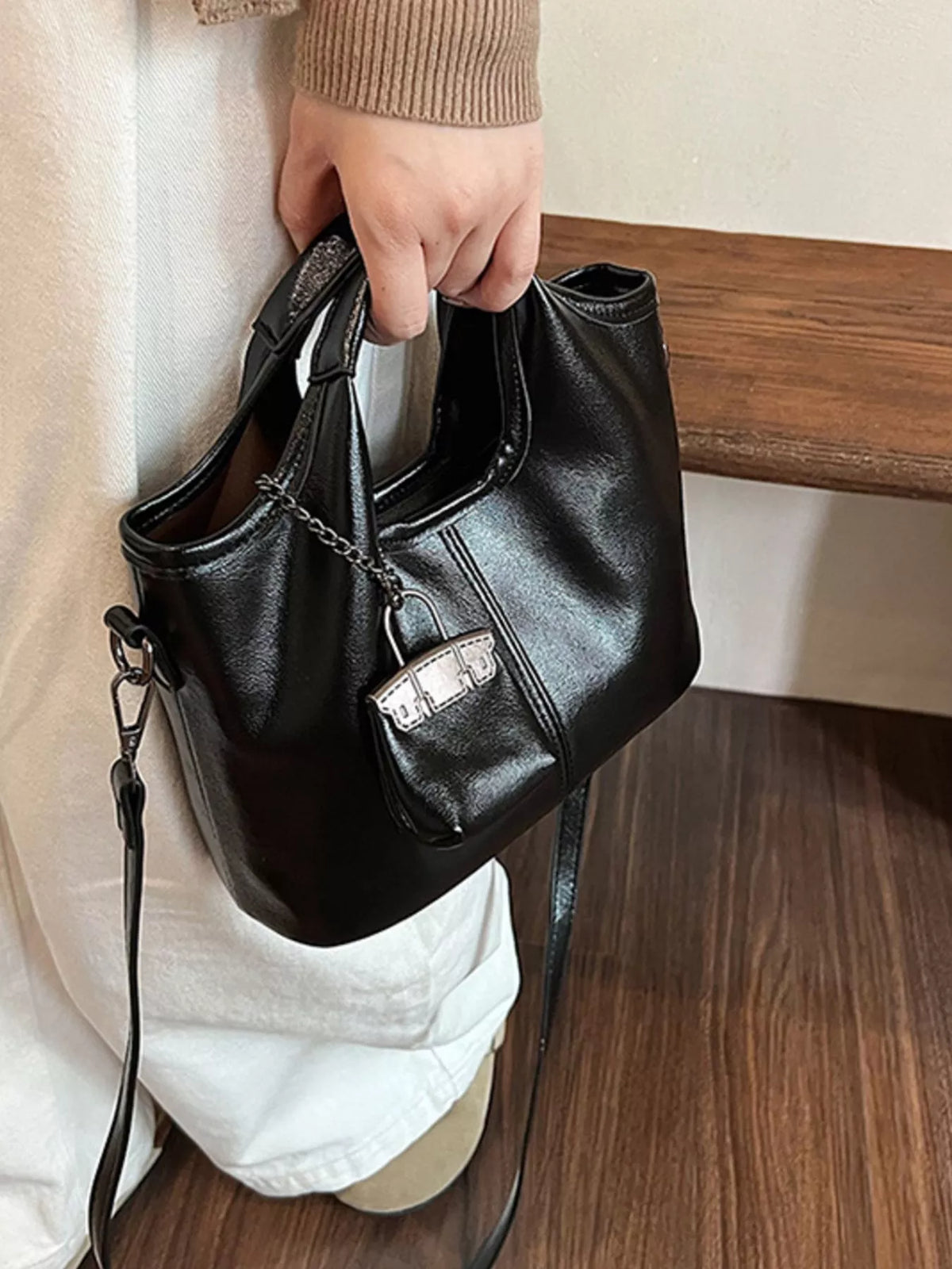 Chic black PU leather crossbody bag with chain detail and mini bag charm.