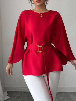 Red belted blouse with batwing sleeves and gold buckle detail, styled with white pants.
