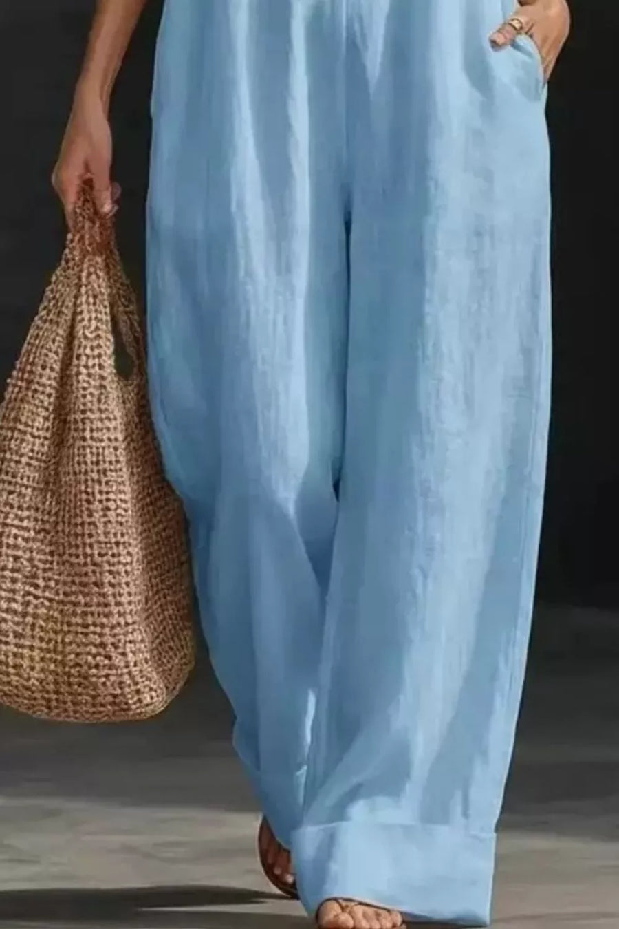 Light blue maternity jumpsuit with pockets and wide legs, shown with a straw tote bag.