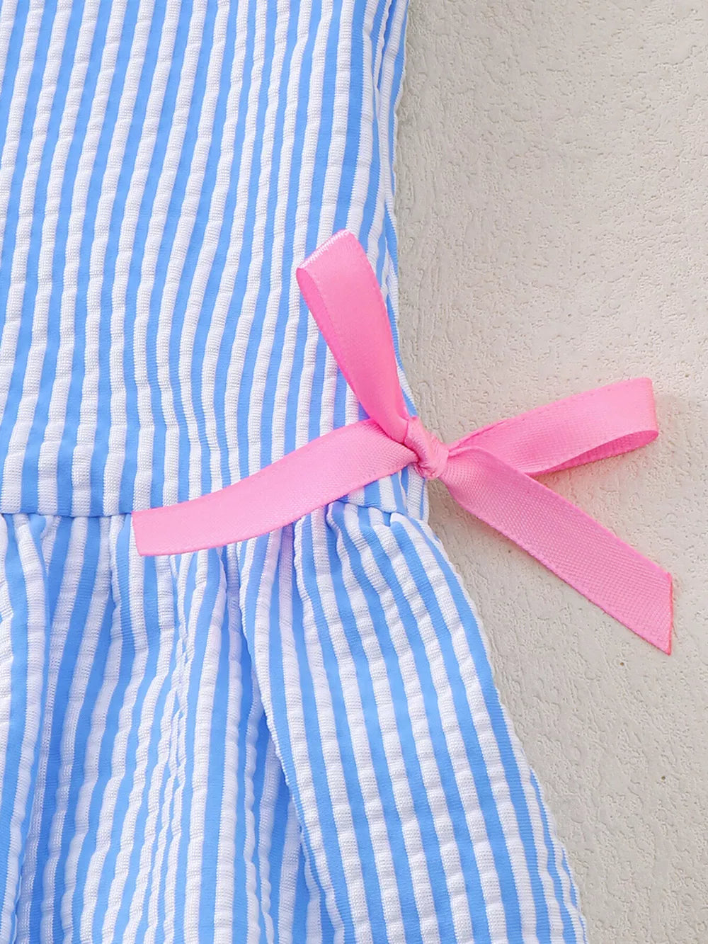 Blue and white striped seersucker one-piece swimsuit with pink side bow detail.