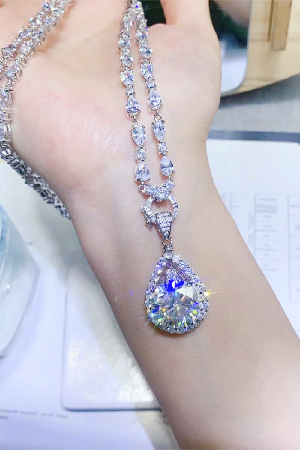 Silver halo moissanite pear drop necklace with a large center stone and pave accents.