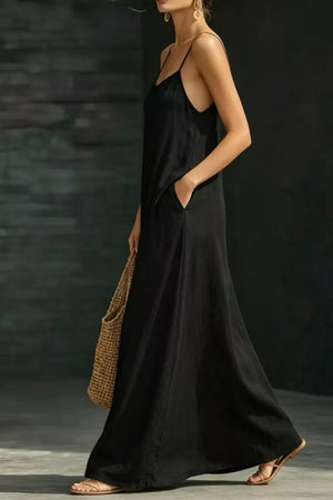 Black A-line maxi dress with spaghetti straps and pockets, styled with sandals and a straw bag.