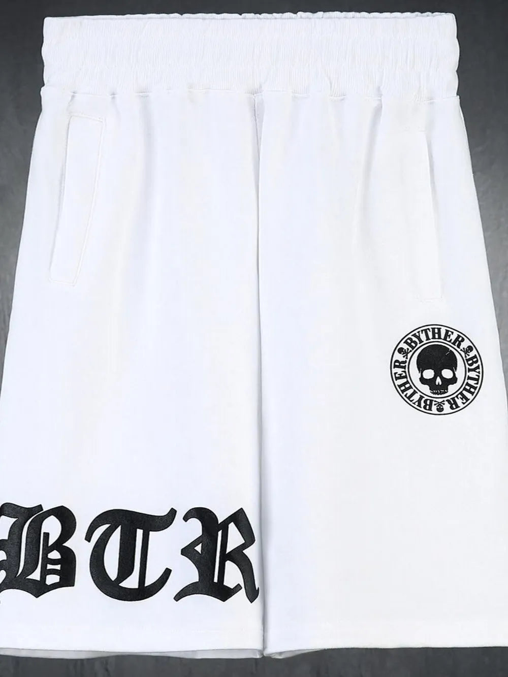 White Gothic script graphic shorts with skull logo detail.