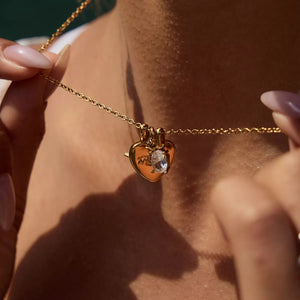 Gold heart charm necklace with crystal accent and engraved "Mom" detail.