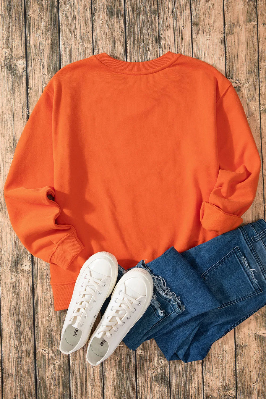 Orange crewneck sweatshirt with cuffed sleeves, styled with blue jeans and white sneakers.
