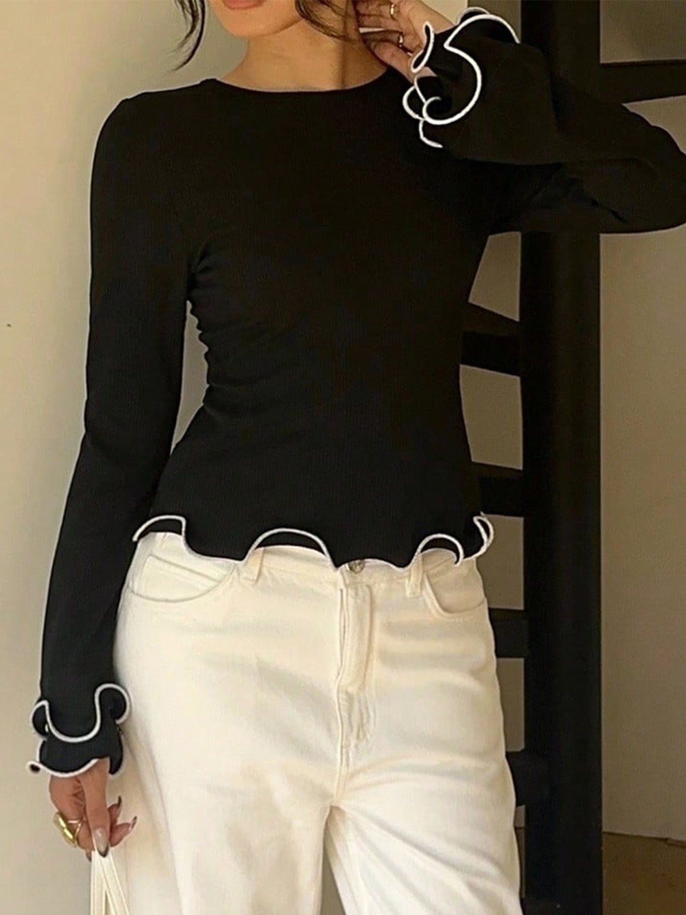 Black crew neck t-shirt with ruffled white trim on sleeves and hem.