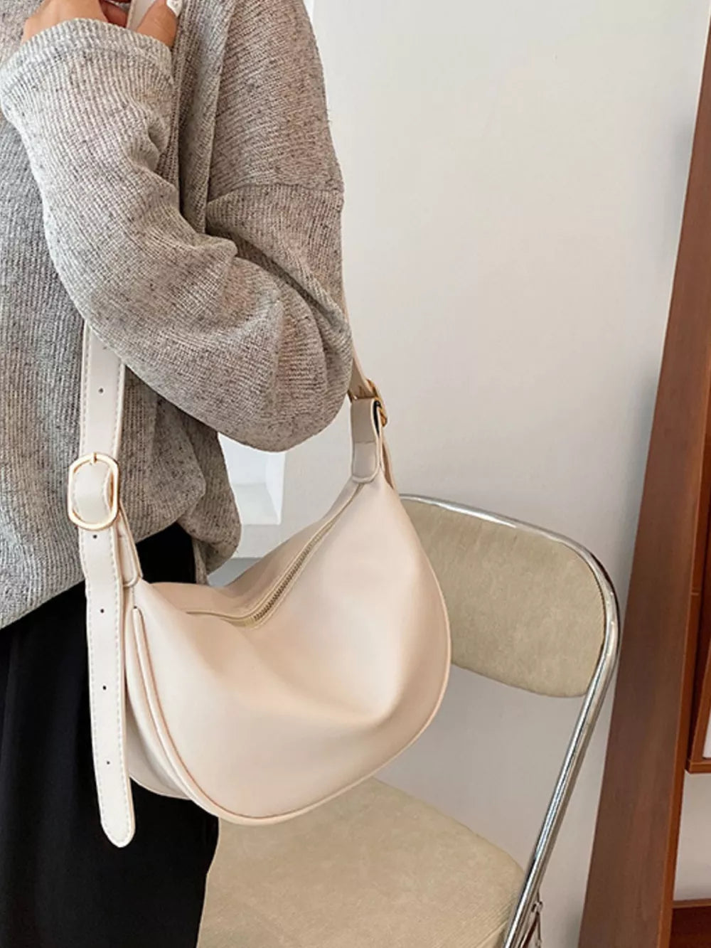 White crescent crossbody bag with adjustable strap and gold buckle detail.