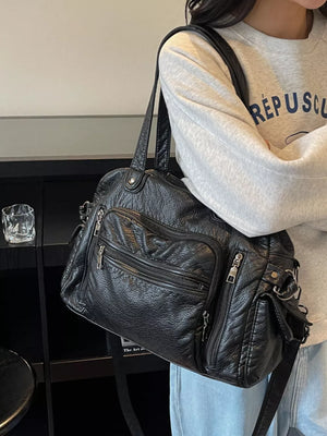 Black faux leather satchel bag with multiple zippered pockets and silver hardware.