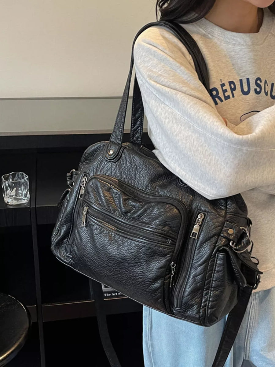 Black faux leather satchel bag with multiple zippered pockets and silver hardware.