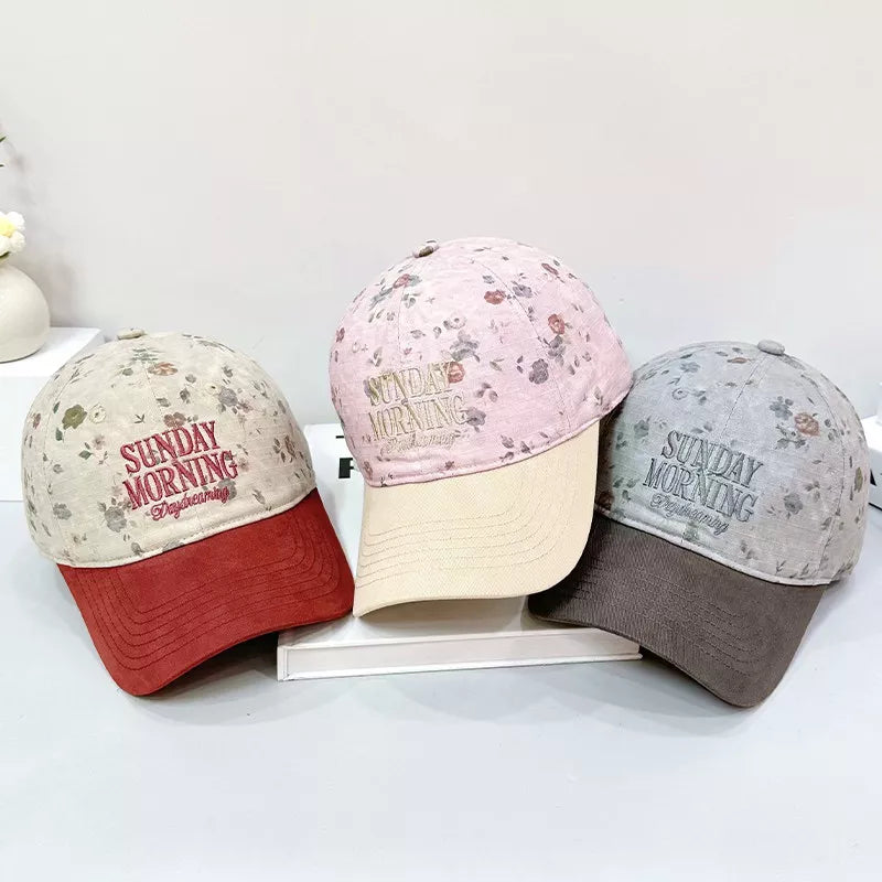 Cotton baseball cap with floral print and embroidered text, available in beige, pink, and grey.
