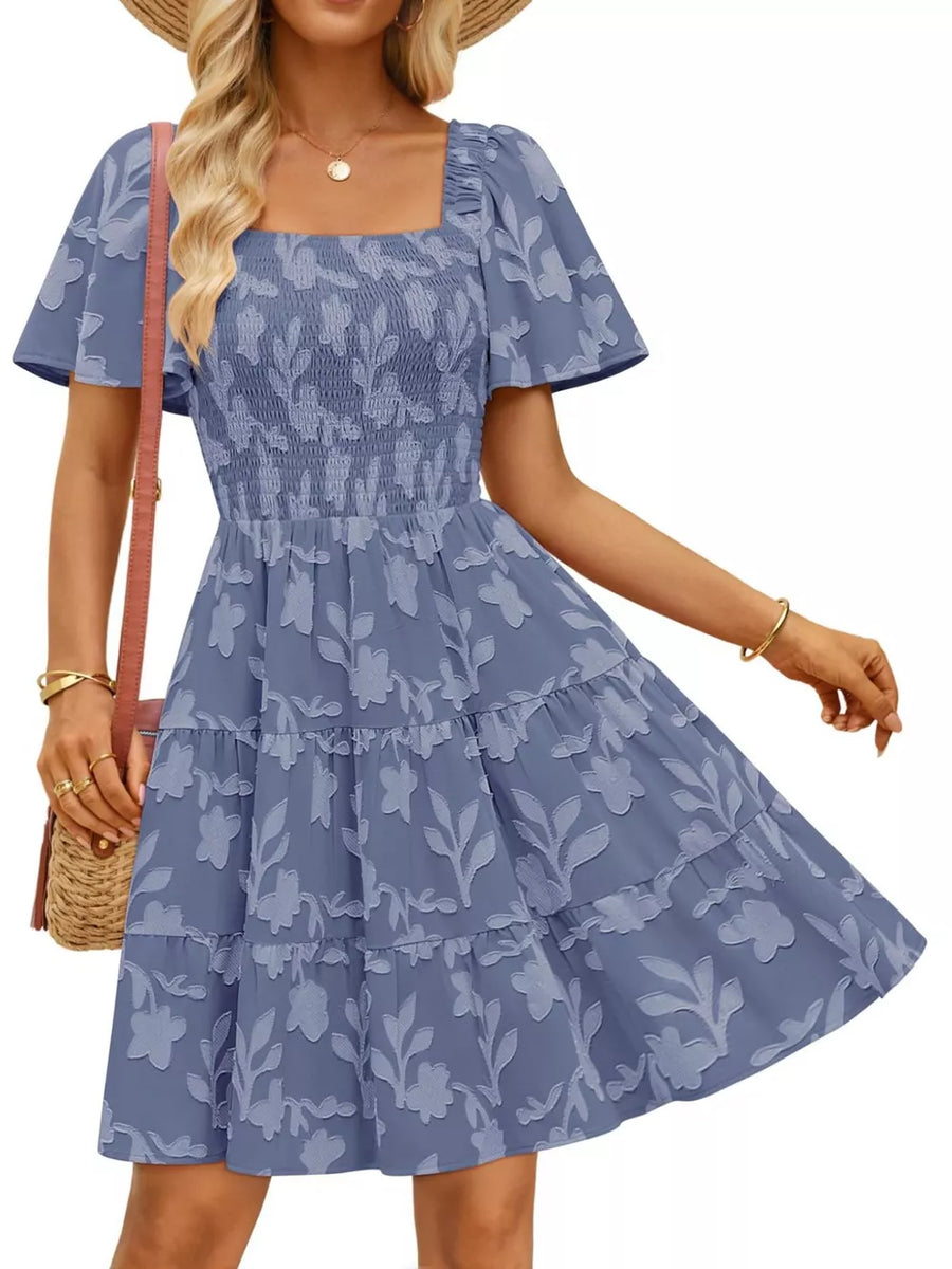 Smocked mini dress in dusty blue with tiered skirt and floral pattern. Square neck, flutter sleeves.