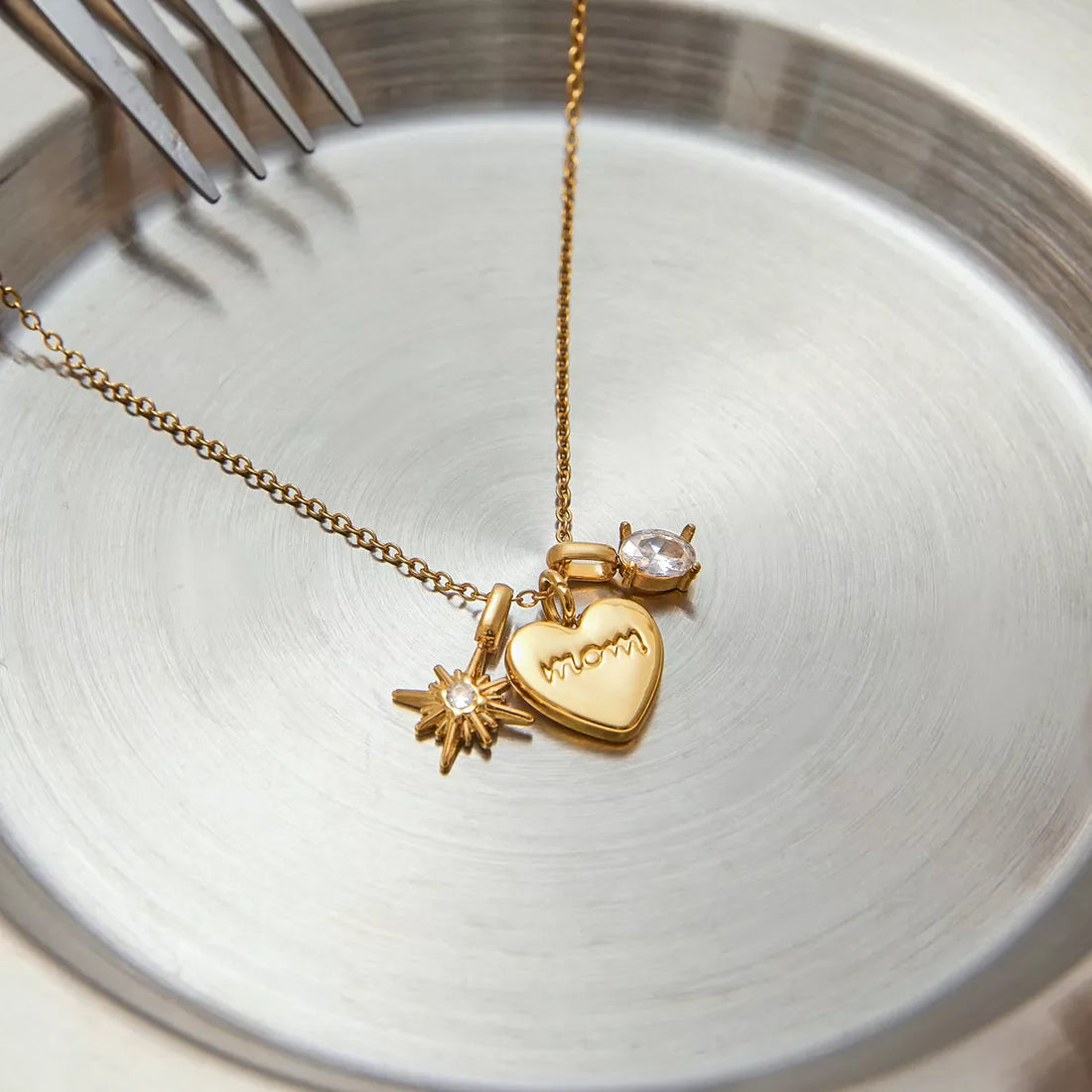 Gold heart charm necklace with MOM engraving, starburst charm, and crystal accent