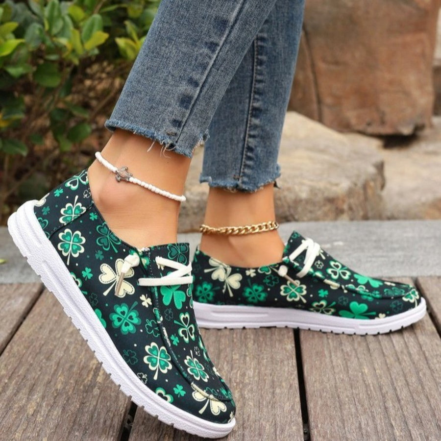 Clover print canvas slip-on sneakers with decorative white laces and white soles.