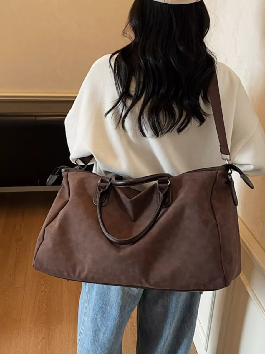 Chocolate brown duffel bag with adjustable strap and twin handles, worn by a woman.