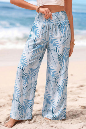 Tropical leaf print wide leg pants in white with blue palm leaves, featuring a smocked waistband.