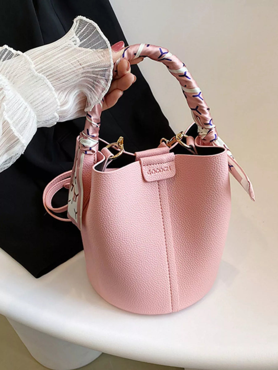 Pink bucket crossbody bag with decorative scarf on handle